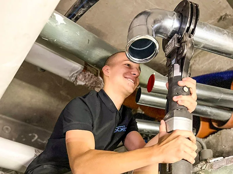 Monteur im Schick-Shirt verpresst eine Rohrleitung an der Decke